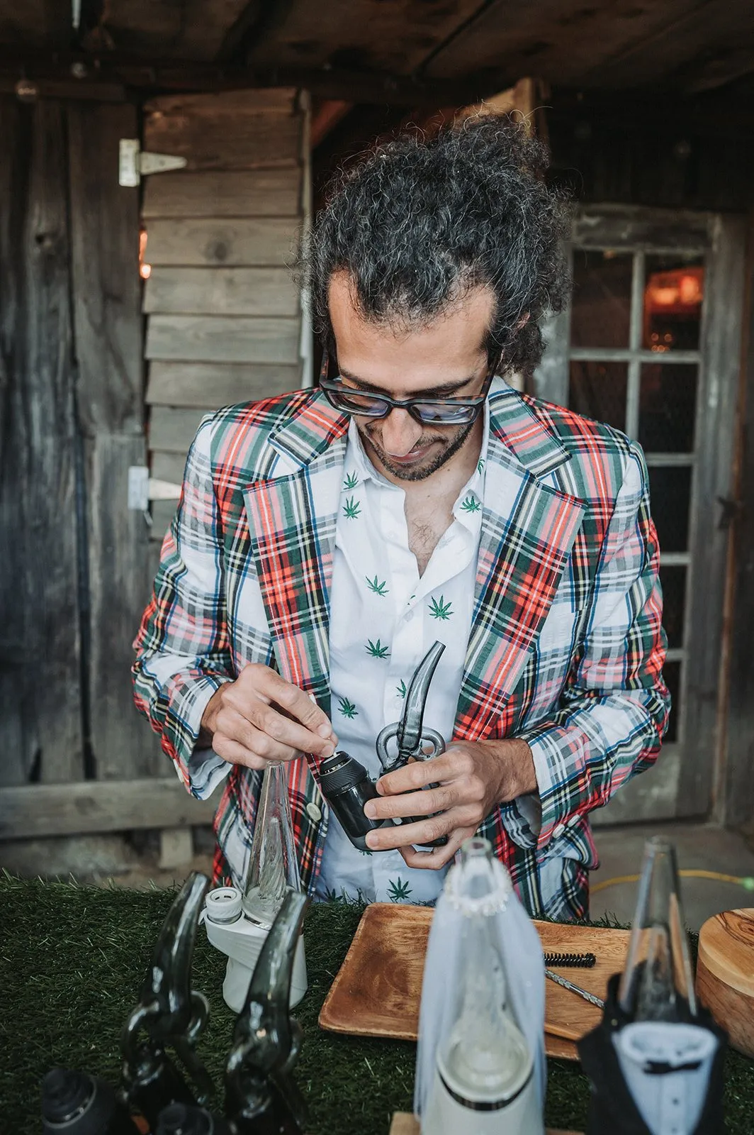 Budtender in a plaid jacket preparing a device behind the cannabis bar at a barn wedding