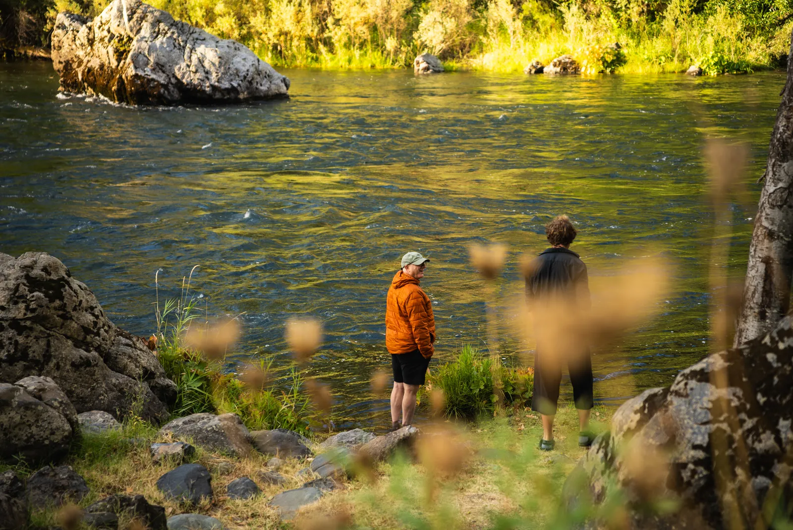 Two retreat guests standing on the rocks along the Trinity River at golden hour