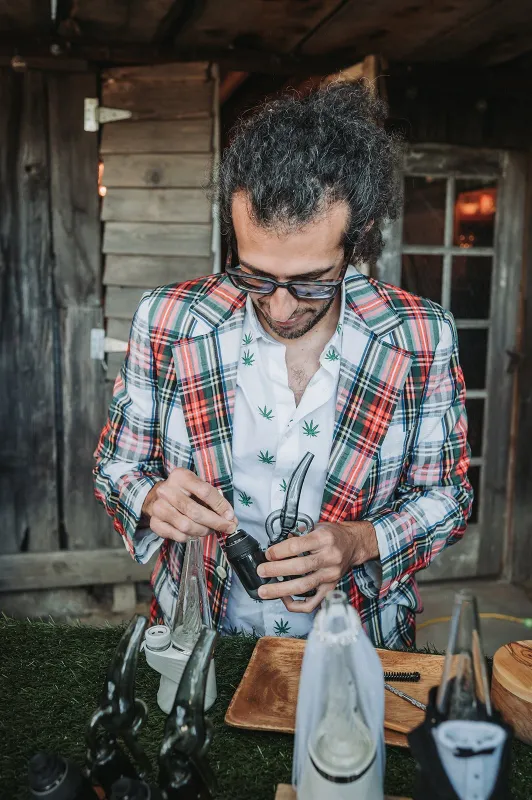 Budtender in a plaid jacket preparing a device behind the cannabis bar at a barn wedding