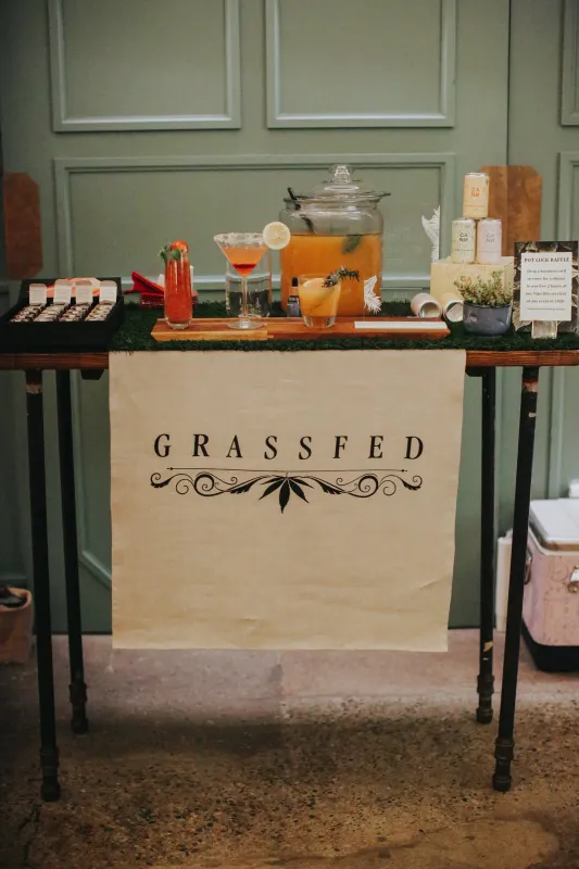 The Grassfed mocktail station with drink dispensers and a menu on a bar draped with a Grassfed banner