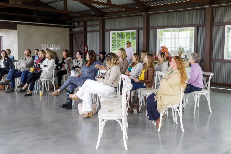 A group seated in rows of white chairs during a Grassfed workshop in a bright event space