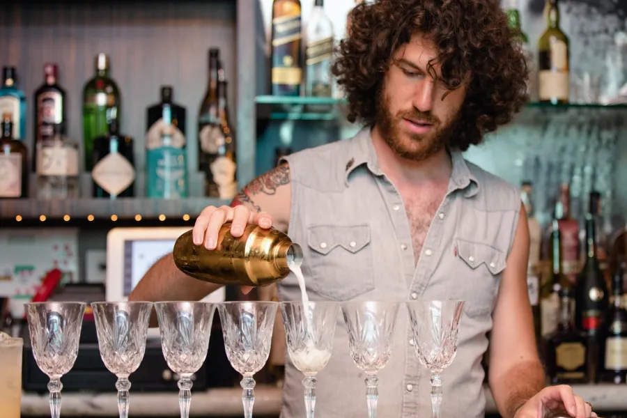 Bartender pouring a drink into a row of crystal glasses