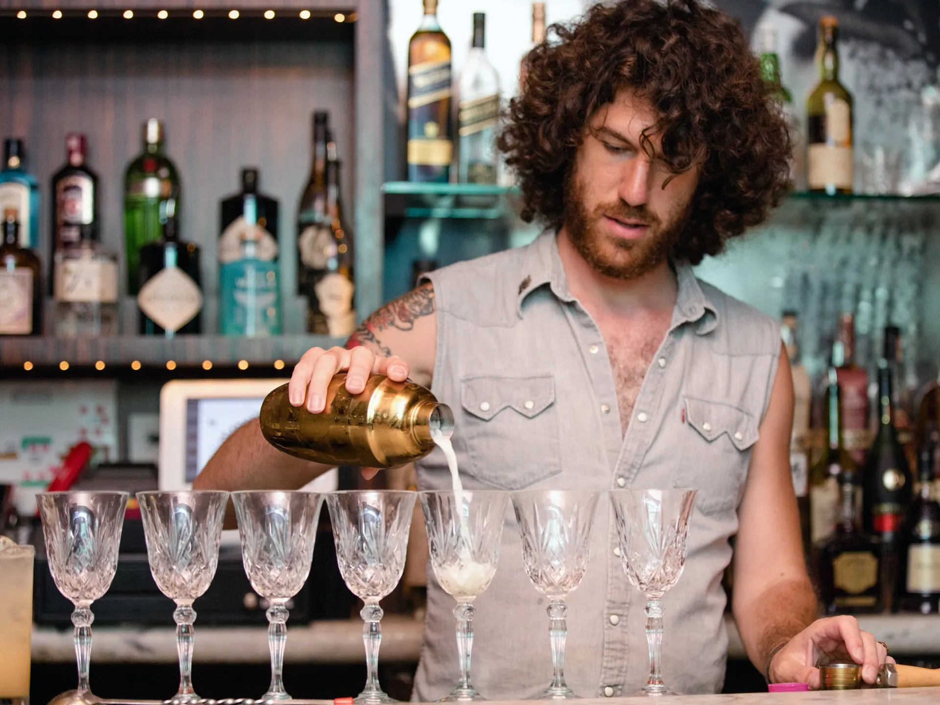 Bartender pouring a drink into a row of crystal glasses
