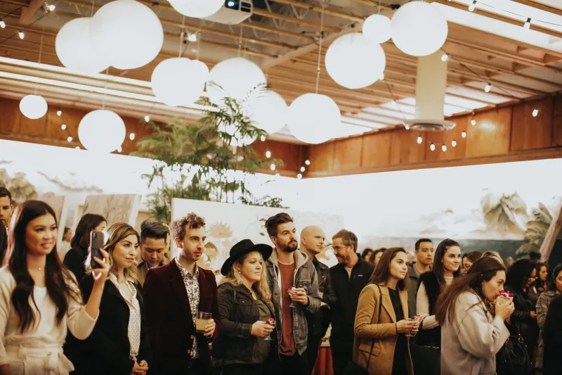 A crowd of guests with drinks under white paper lanterns at an indoor event