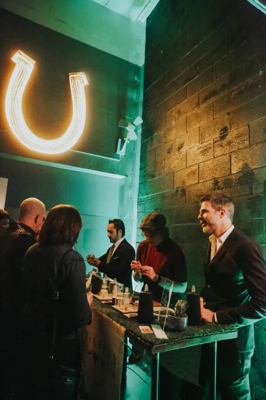 Guests at a cannabis bar lit in green, under a glowing neon horseshoe sign