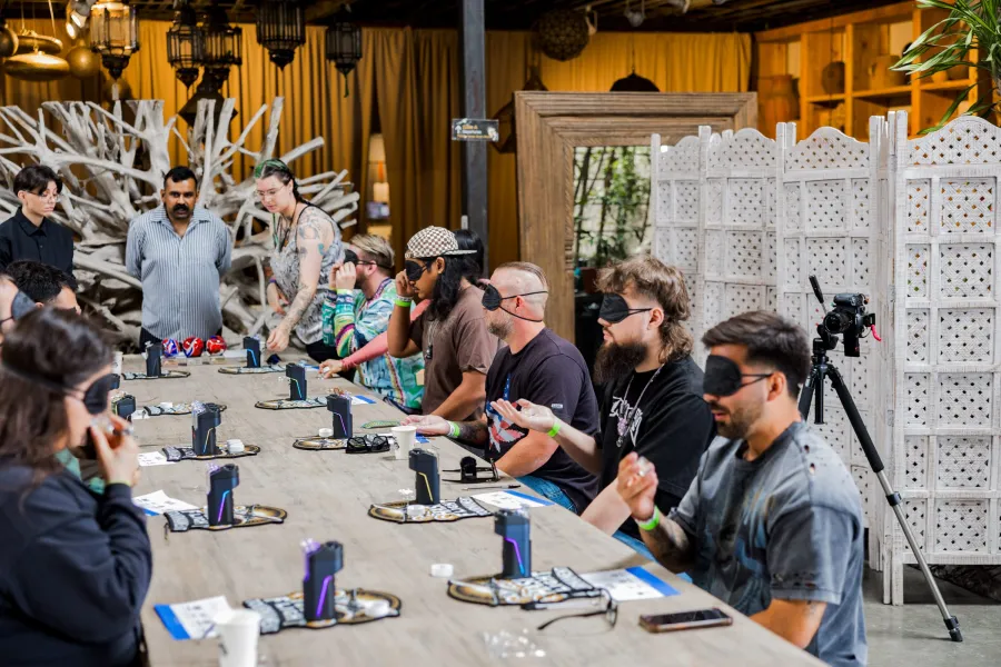 Competitors in eye masks smelling hash samples along a long wooden table at the Hash Flight Tournament