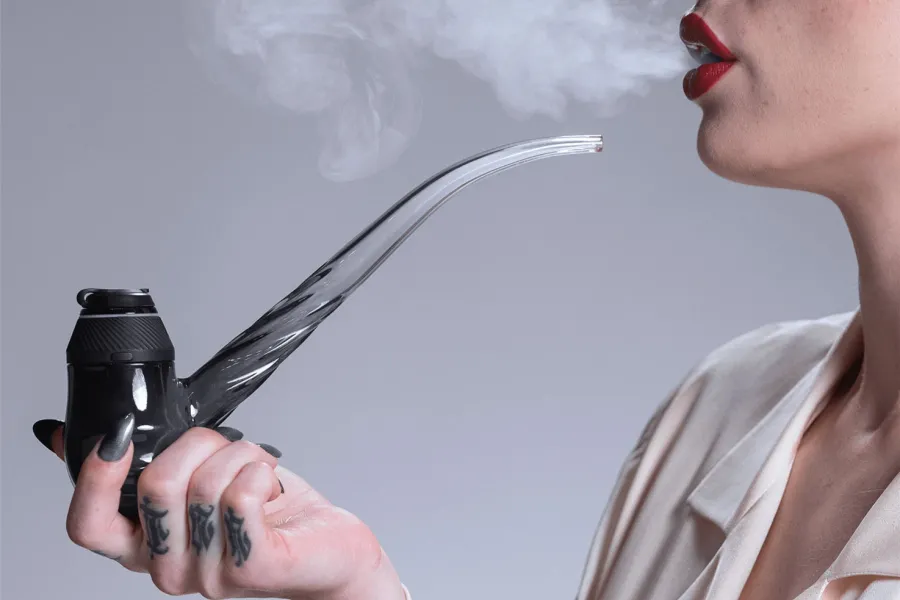 A woman exhaling vapor while holding a dab device with a curved glass mouthpiece