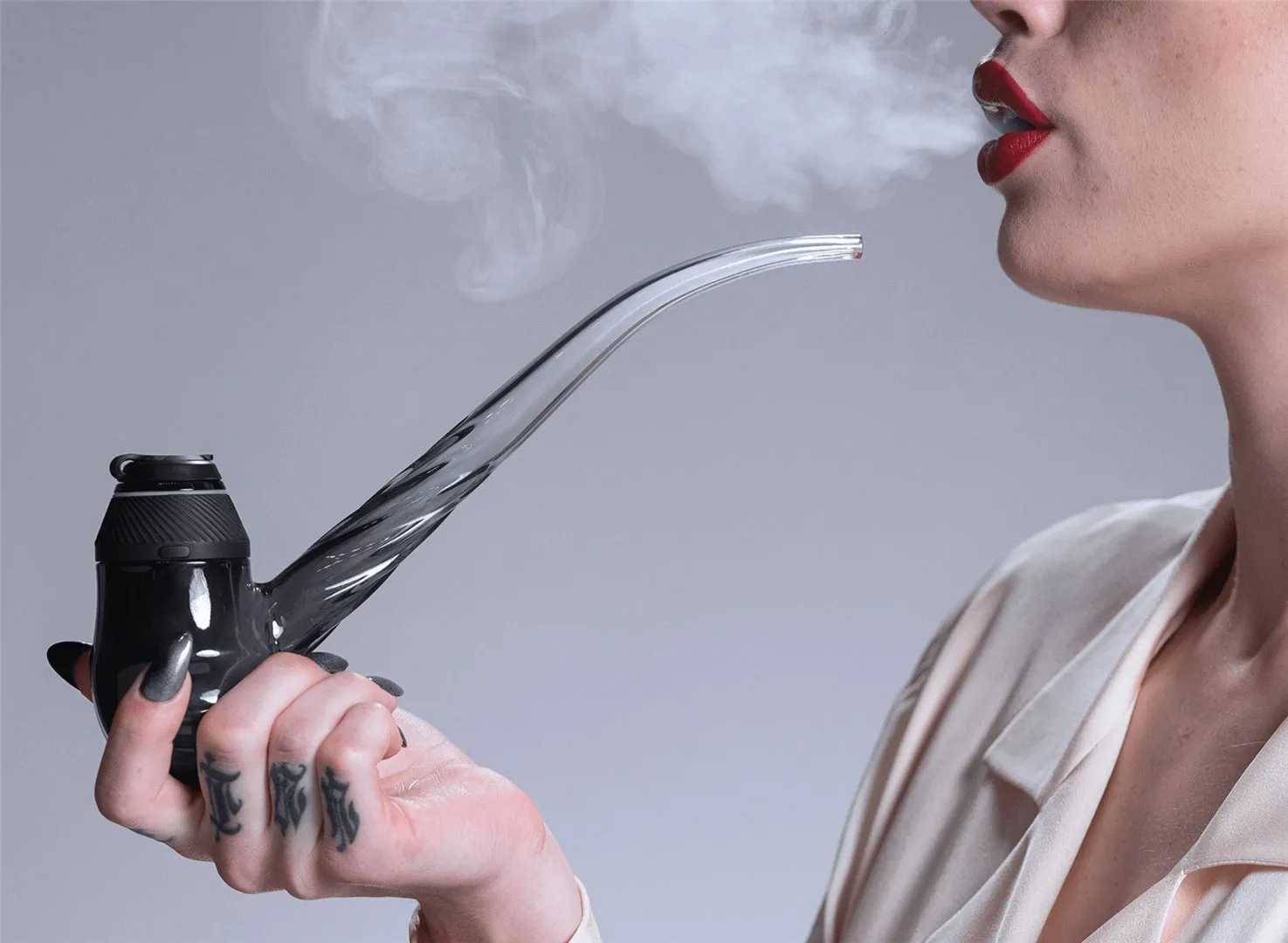 A woman exhaling vapor while holding a dab device with a curved glass mouthpiece