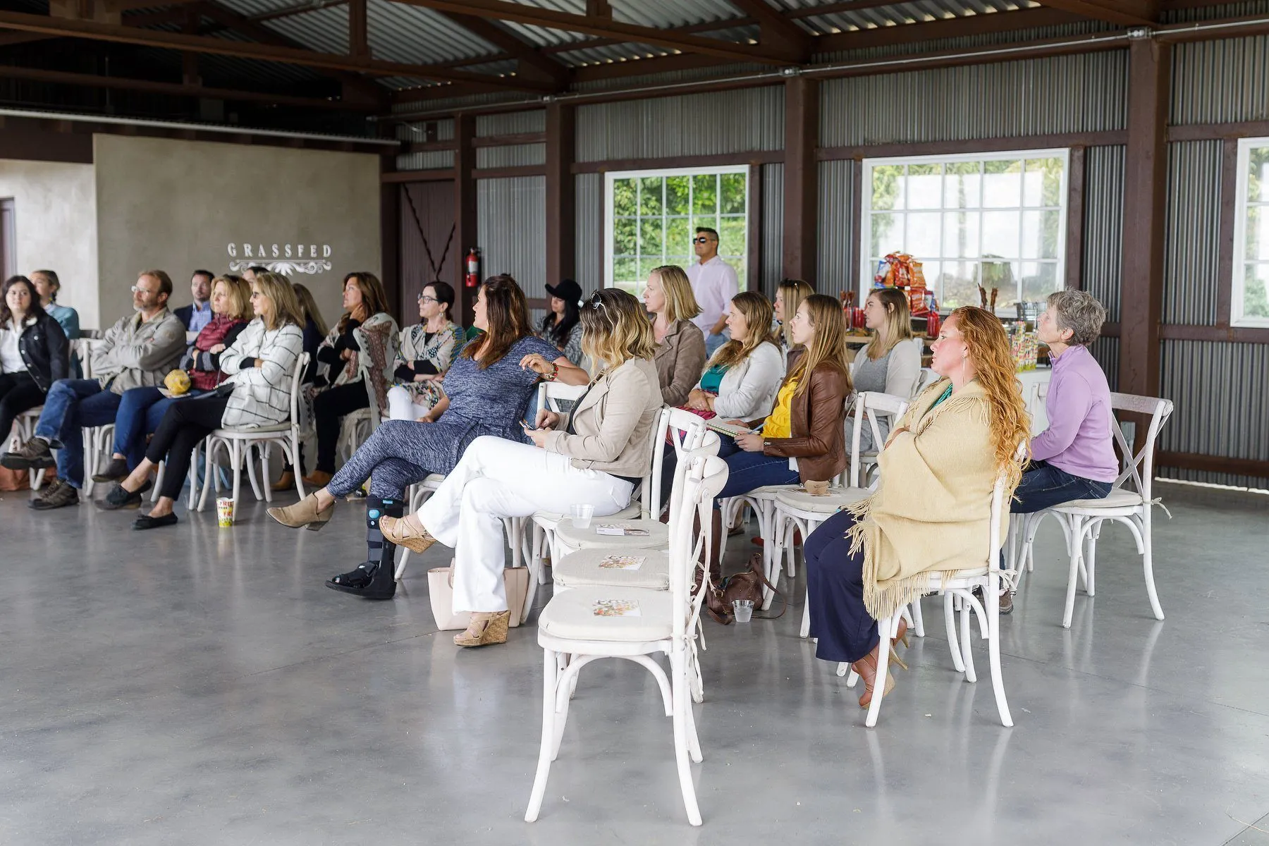 A group seated in rows of white chairs during a Grassfed workshop in a bright event space