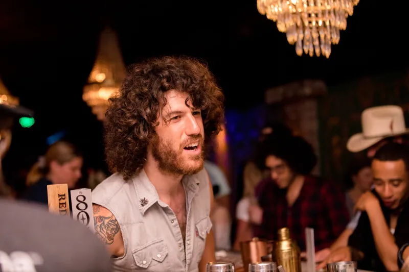 A curly-haired guest laughing at the bar under glowing chandeliers