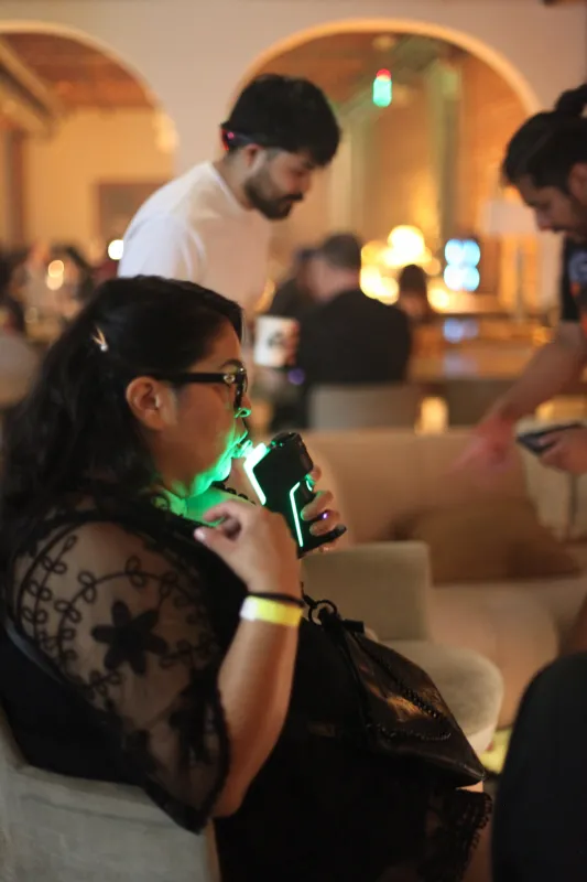 A guest in glasses inhaling from a glowing green vaporizer at an evening hash tasting