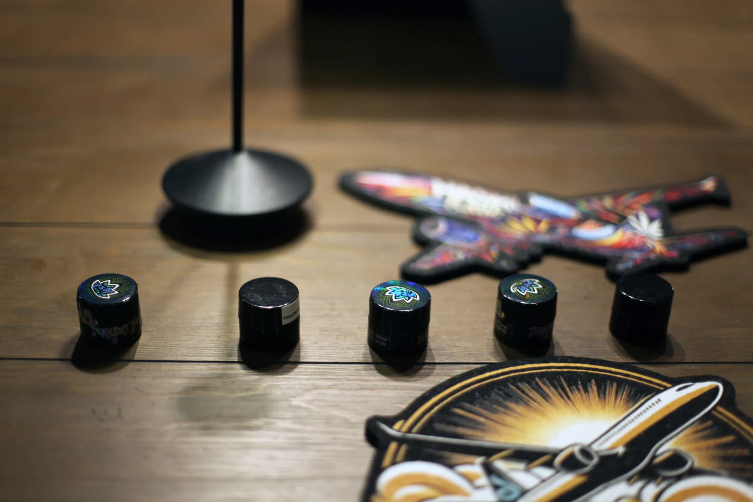 Five small black jars of hash in a row on a wooden table beside Hash Flight patches