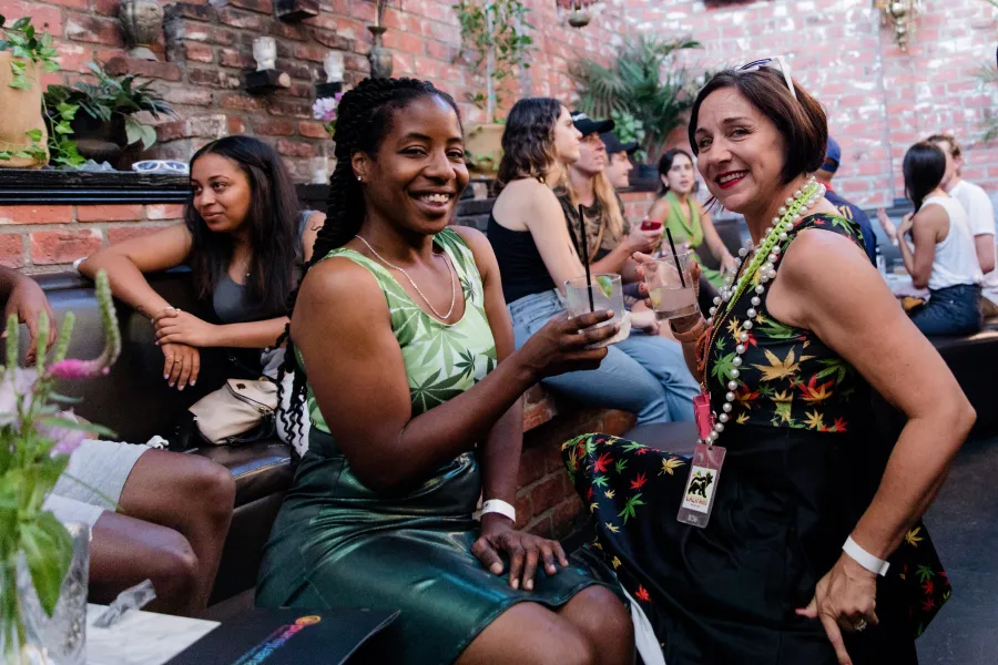 Smiling guests in green outfits raising drinks in a brick courtyard