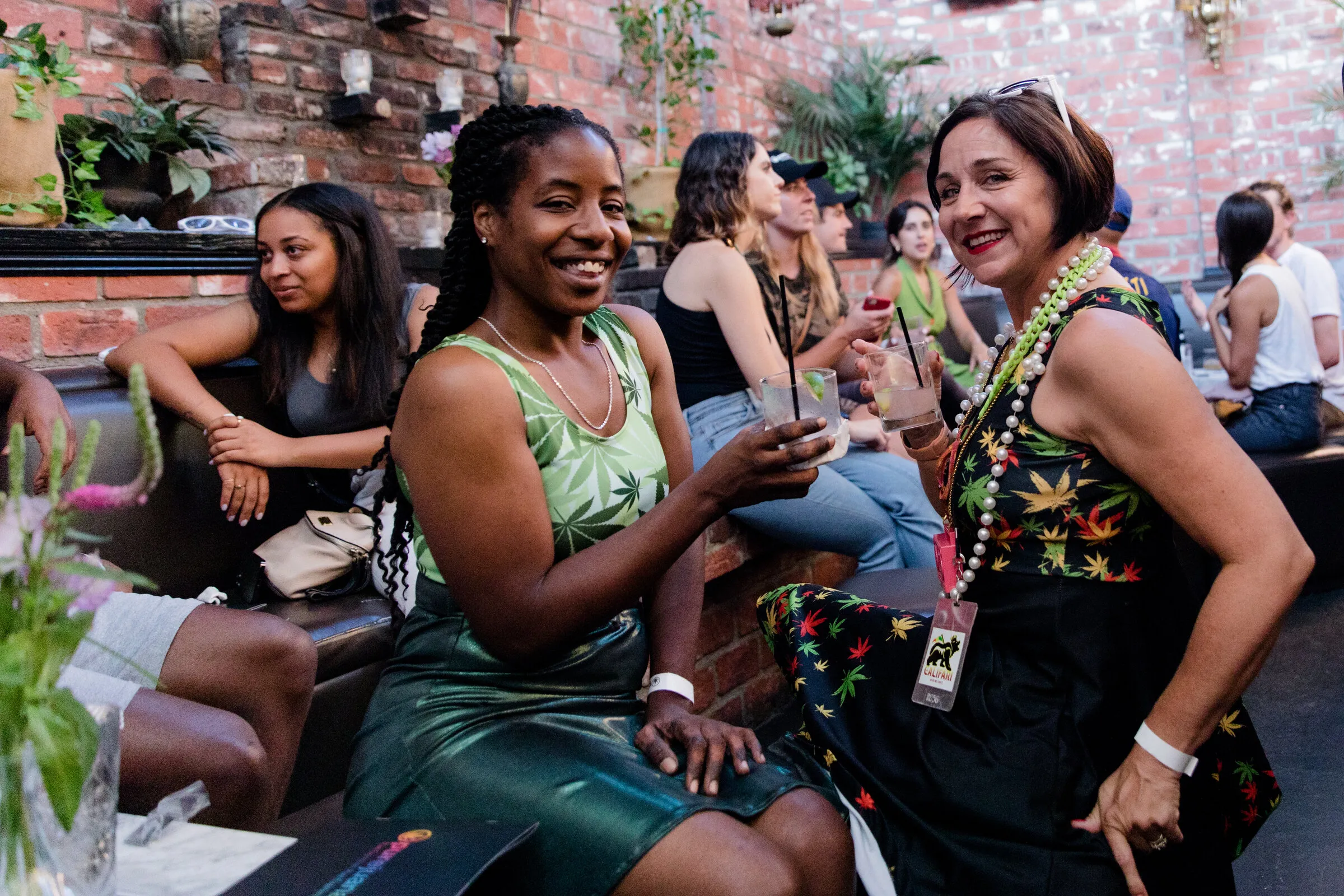 Smiling guests in green outfits raising drinks in a brick courtyard