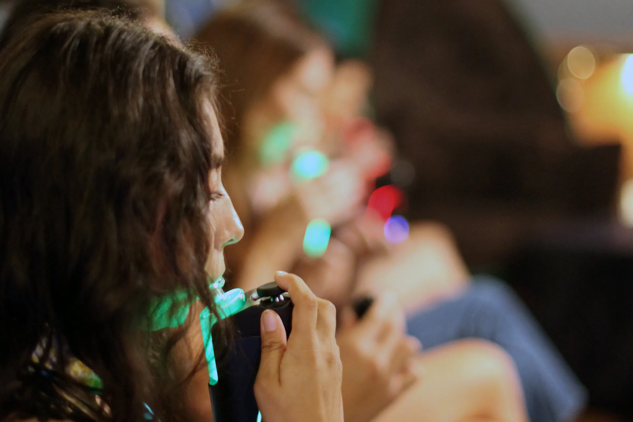 Guest tasting from a glowing device at a Hash Flight tasting, other guests seated behind her