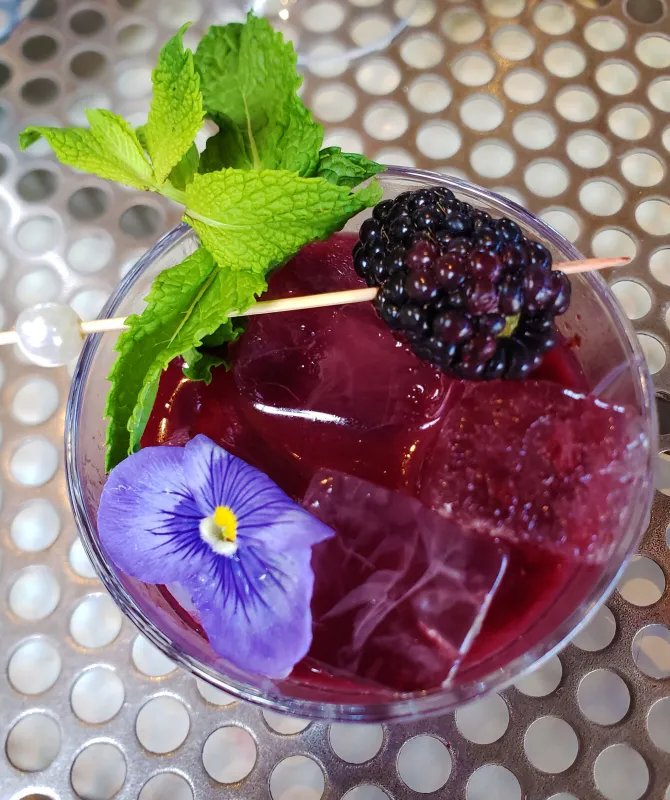 A deep purple mocktail with blackberries, mint and a pansy garnish