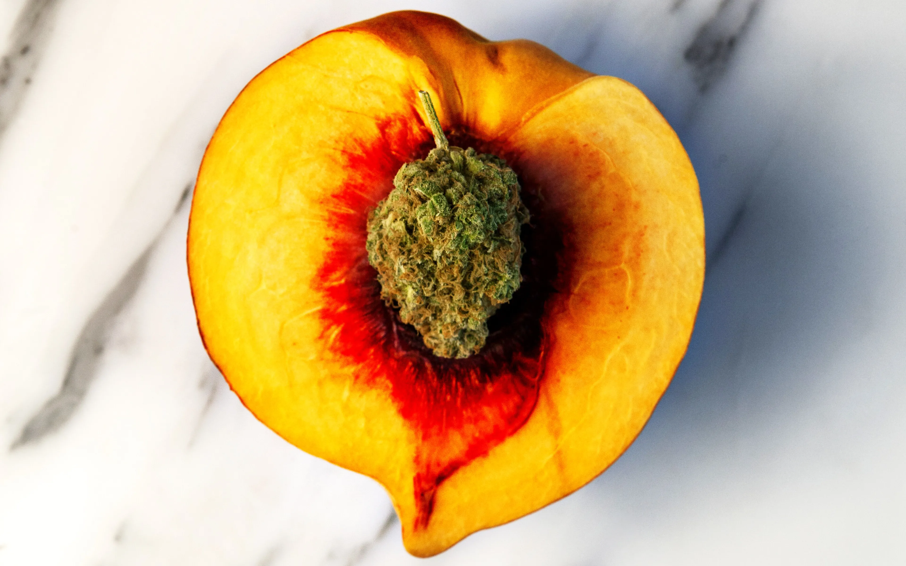 A cannabis flower set in the pit of a halved peach on white marble